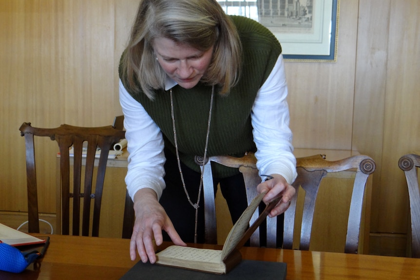 A woman leans over a small notebook that rests on a wooden table.