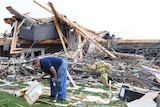 A man picking up a piece of debris in front of a destroyed house. 