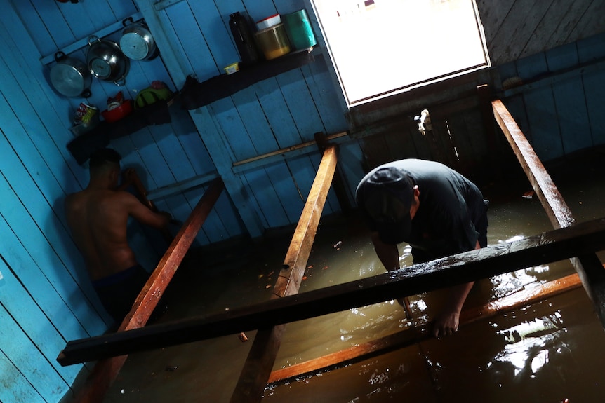 Men nail up wooden planks as a raised floor as floodwater rises in their home