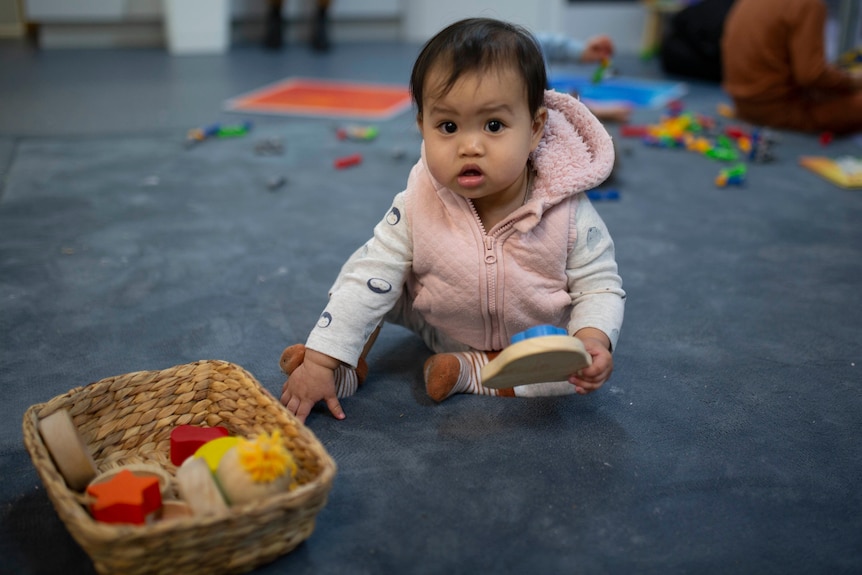 A baby in a pink suit sits on a floor