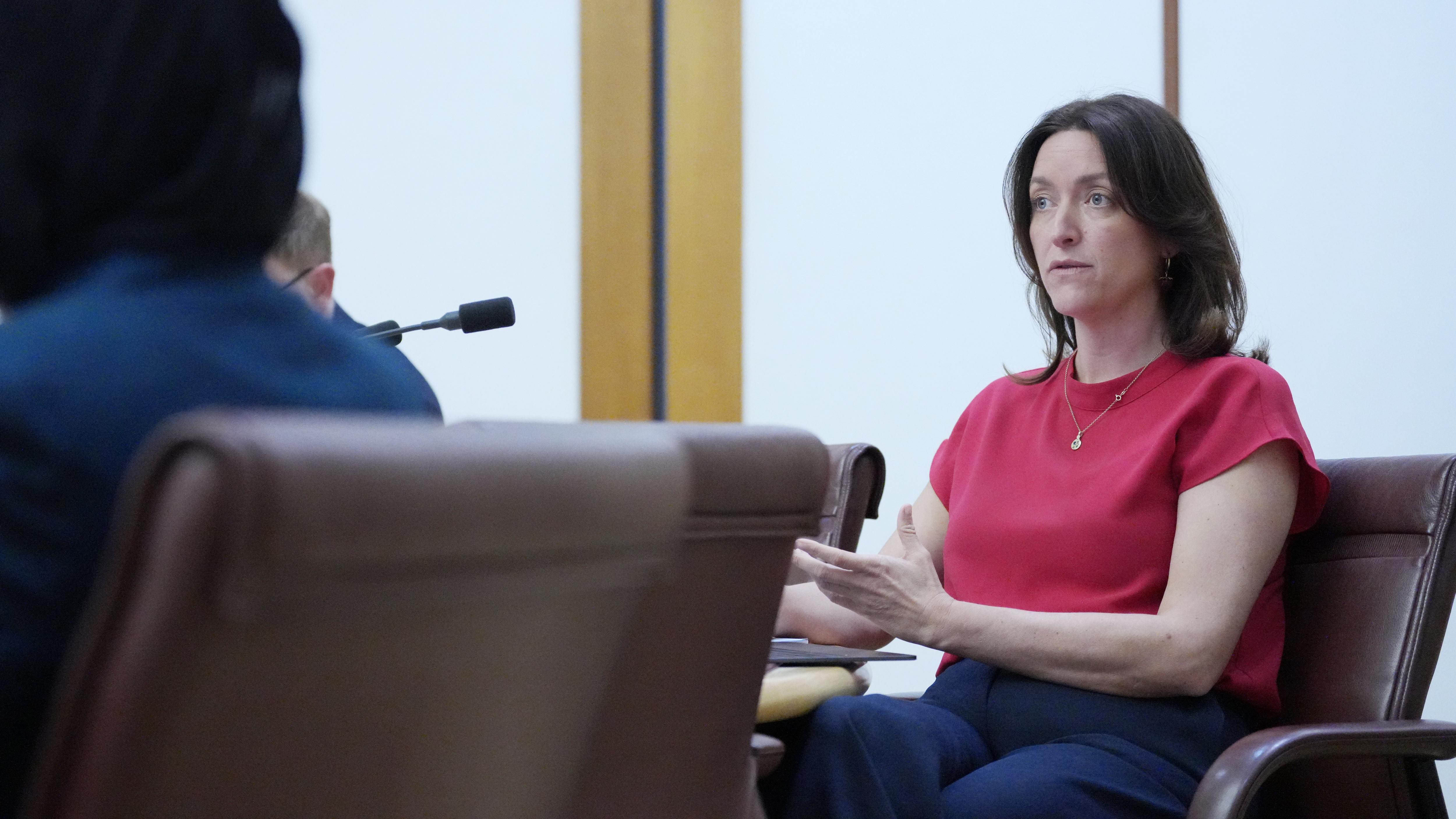 A woman in a red top asks questions at a senate hearing.