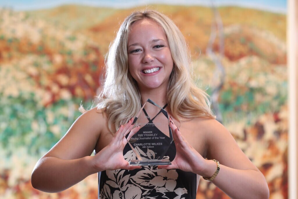 A young woman smiles as she holds up an award.