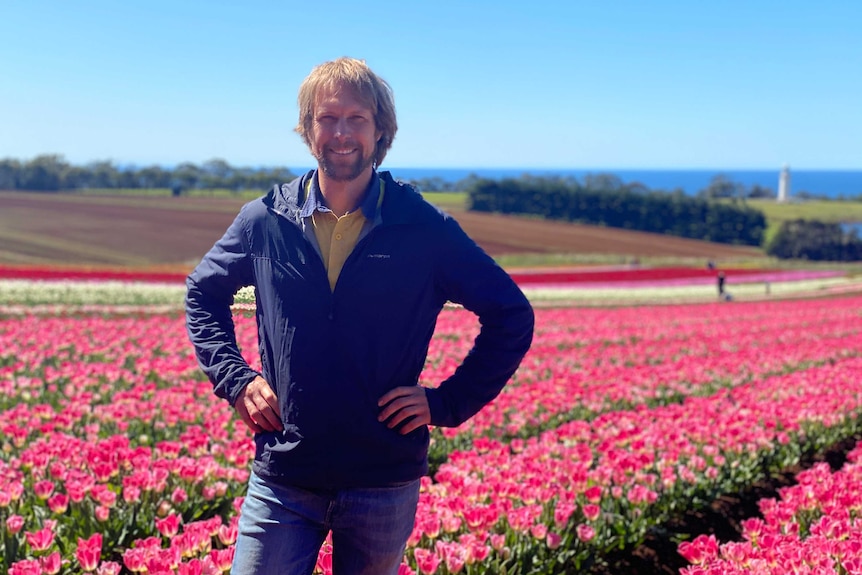 A man smiles with hands on his hips in a field of tulips.