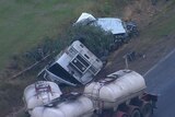 An aerial shot showing the mangled wreck of a truck on the side of a highway.