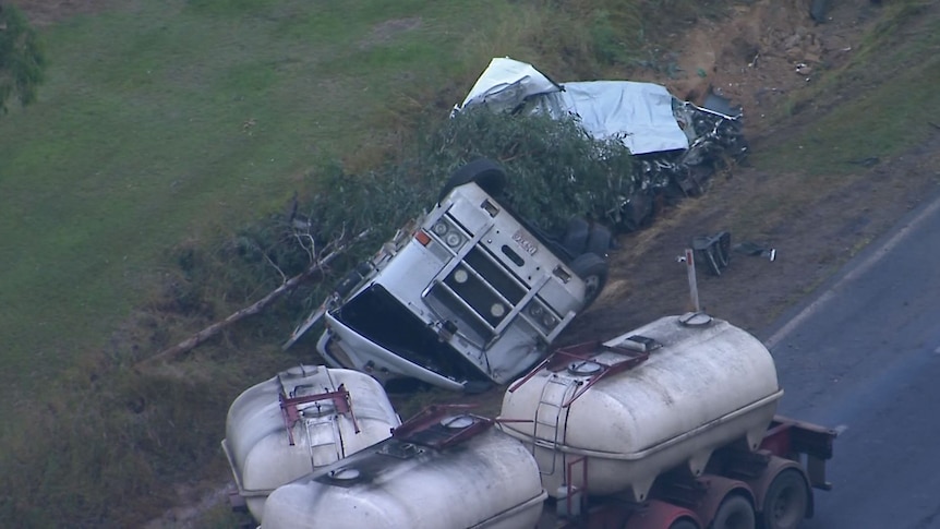 An aerial shot showing the mangled wreck of a truck on the side of a highway.