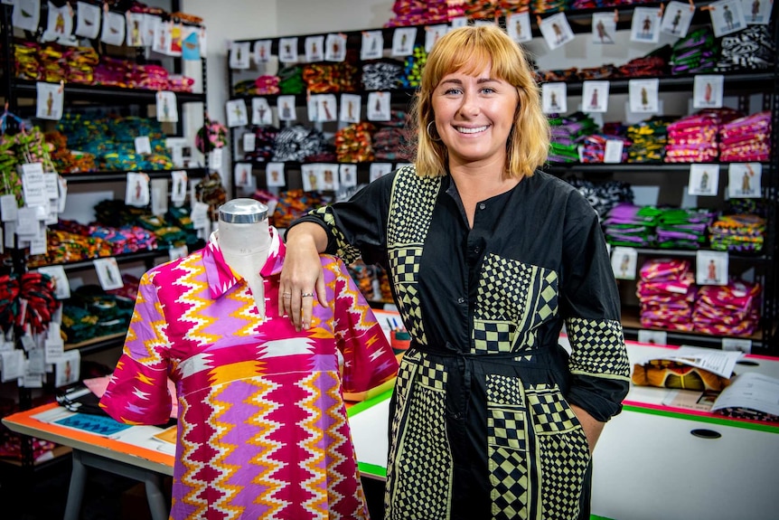 Anna Roberston stand next to a mannequin, with clothing samples behind her.