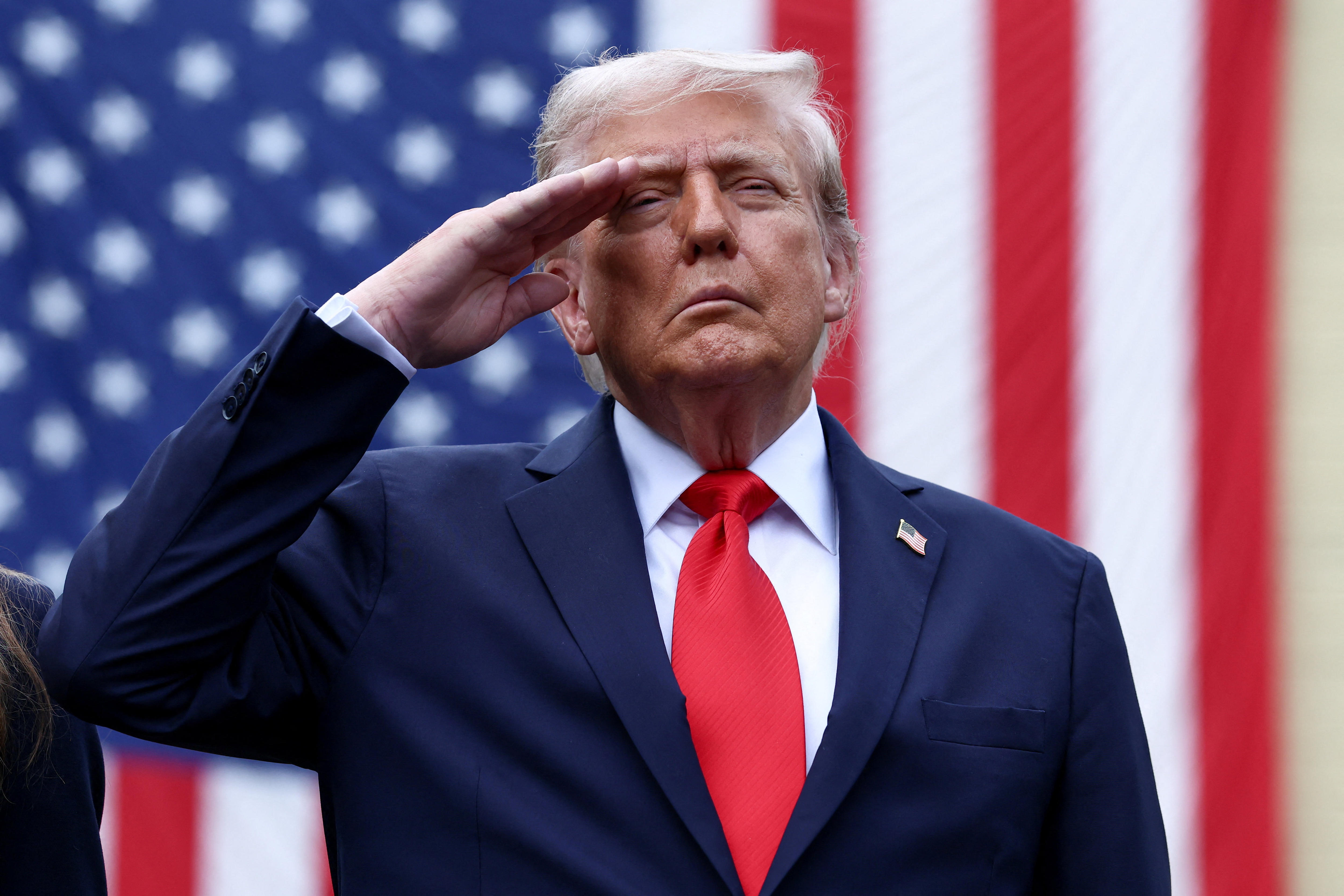 Trump stands in front of a US flag saluting