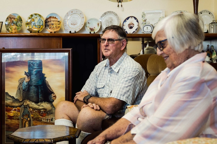 Bob Lockley talks while sitting on the lounge as Kaye sits next to him smiling.