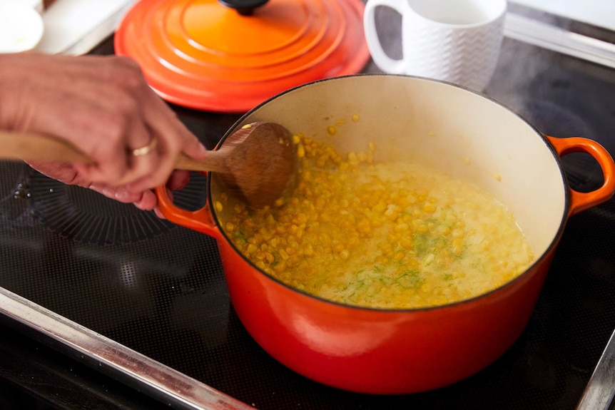 Corn kernels in a Dutch oven cooking being cooked with cream, parmesan, lime zest and butter, a creamy pasta dinner.