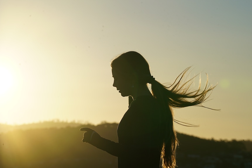 The silhouette of a woman with long hair running under a blue sky.