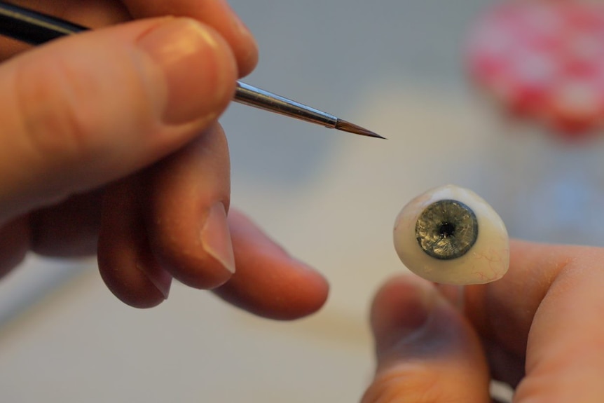 A close-up of a brush painting a prosthetic eye
