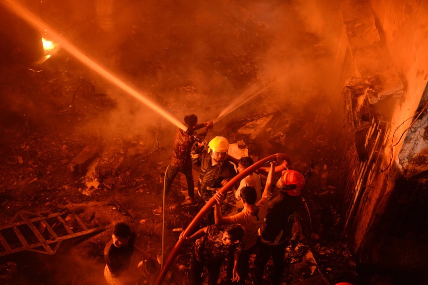 Firefighters stand amid rubble hosing a raging fire in Dhaka, Bangladesh