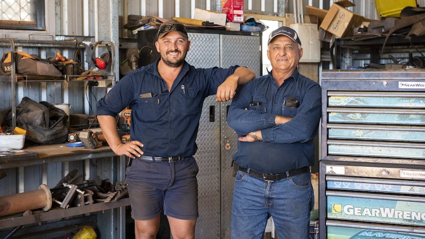 Wide shot of father and son in farm work gear standing in a shed