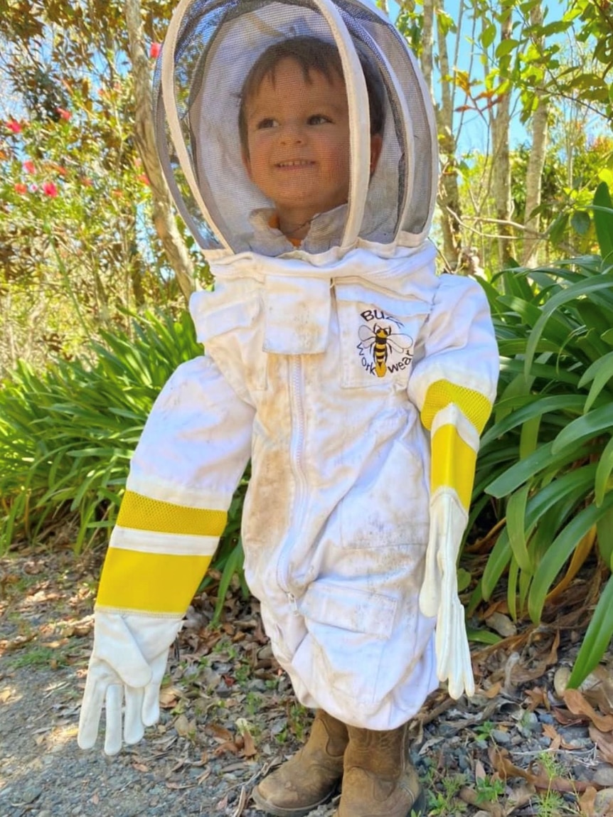 Three-year-old Sterling Cannon stands in a beekeeper suit, which includes oversized gloves.
