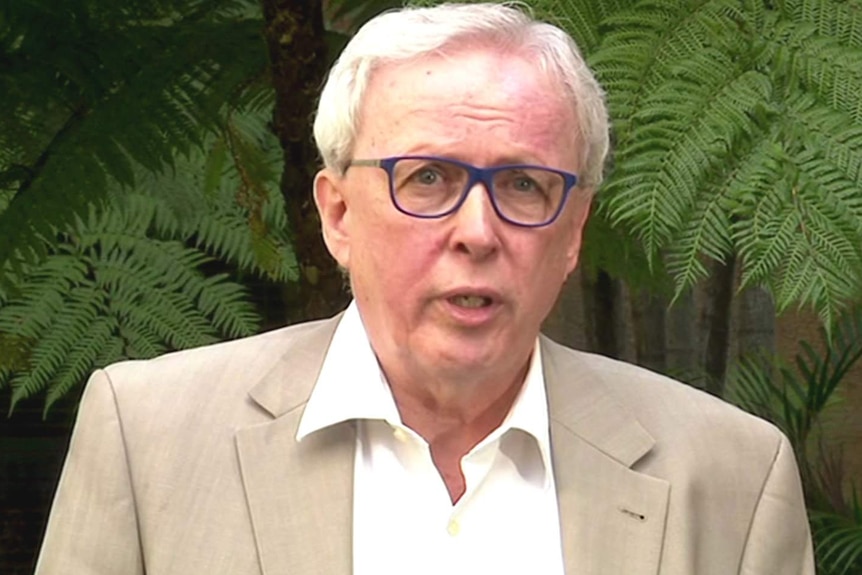 A man in a collared shirt and coat speaking in a garden