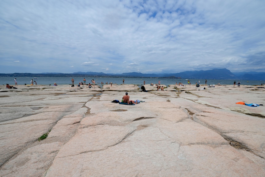 A side view of people sunbathing on rocks at Lake Garda