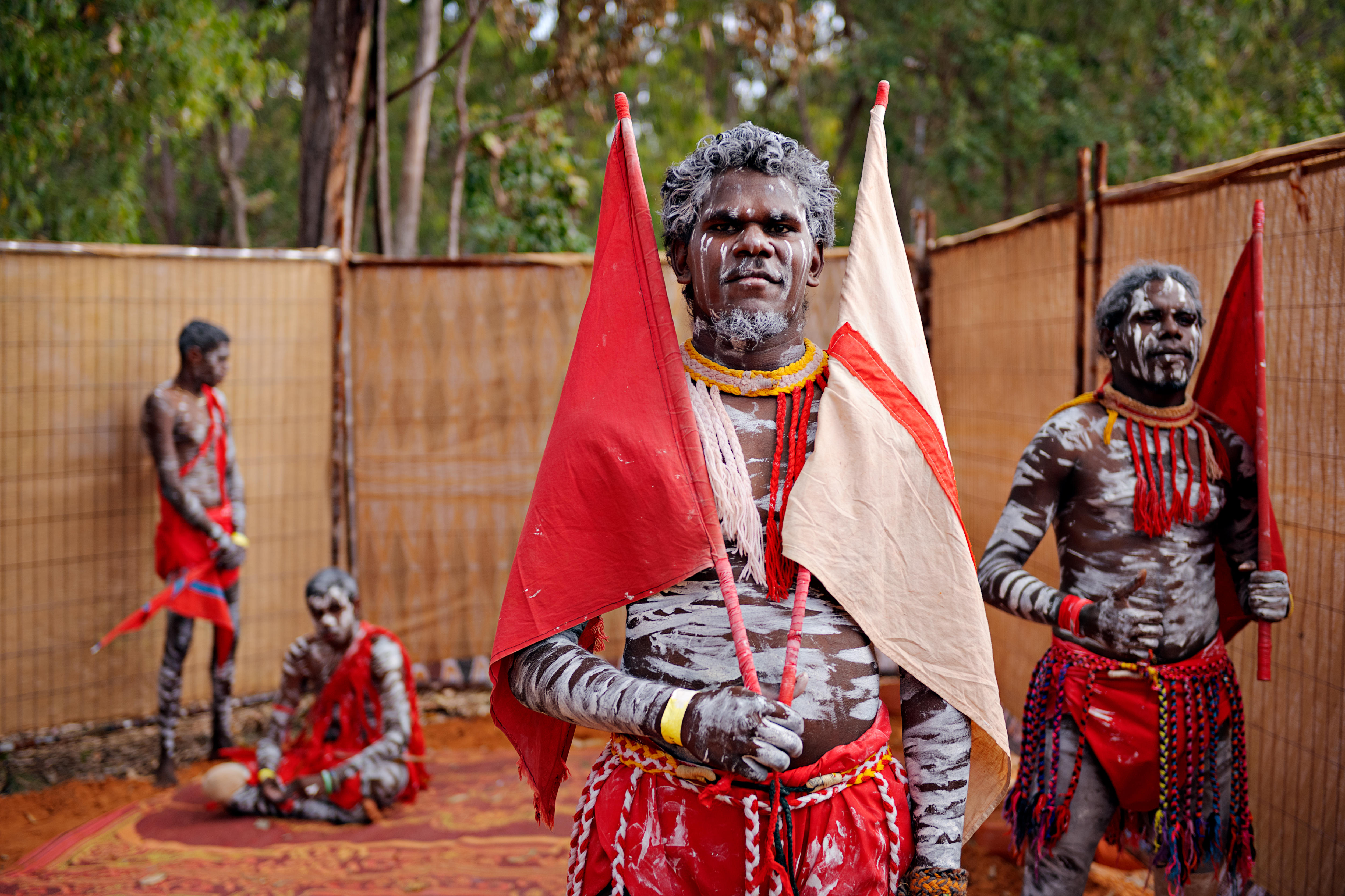 An Indigenous man wearing traditional face painting and carrying red and white flags.