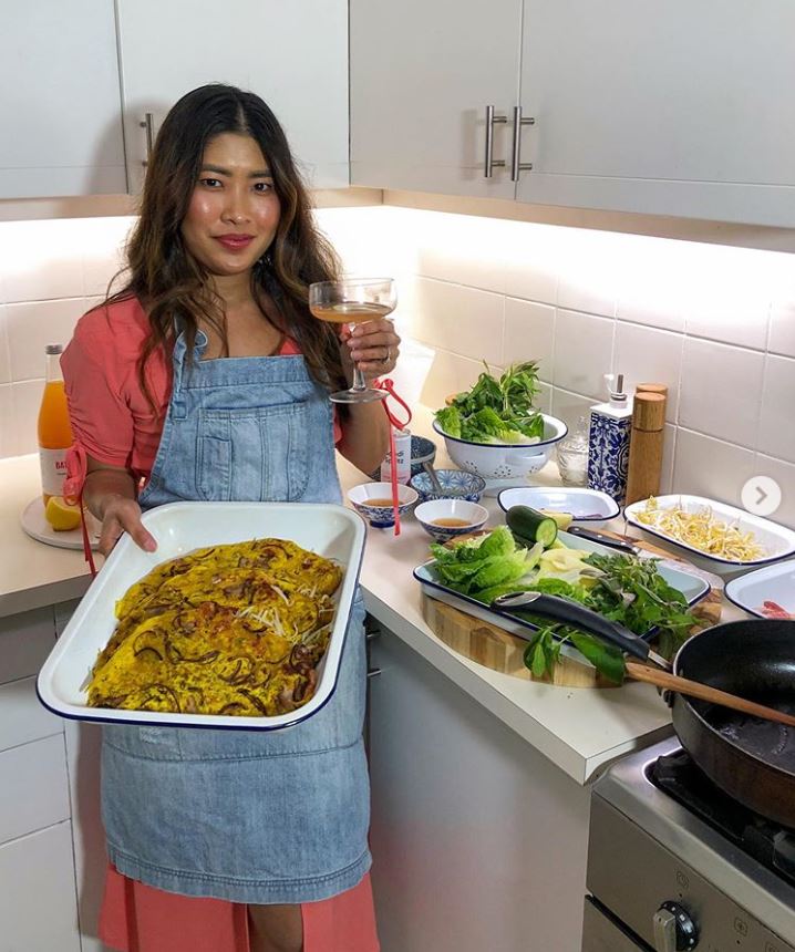 A woman wearing a denim apron holding a tray of food