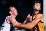 A North Melbourne AFL player pushes against a Hawthorn opponent as they prepare to contest for the ball.