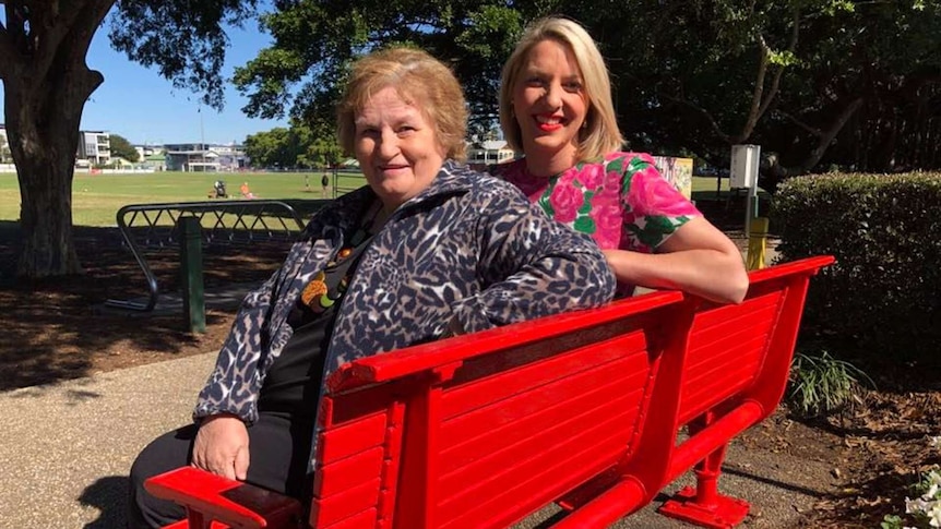 Two ladies sitting on a bright red bench.