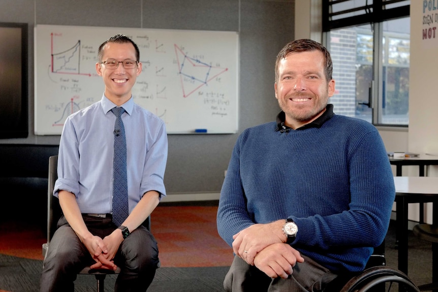 Eddie Woo and Kurt Fearnley sit smiling in a school classroom.