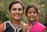 Mother and young daughter in traditional Indian dress smile at the camera.