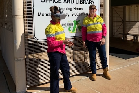 A female council worker is wearing a virtual reality headset, holding a controller while a colleague watches on.