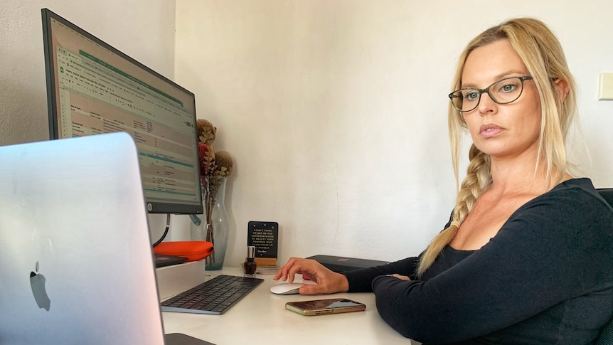 A woman looks at a laptop screen while seated at a desk.