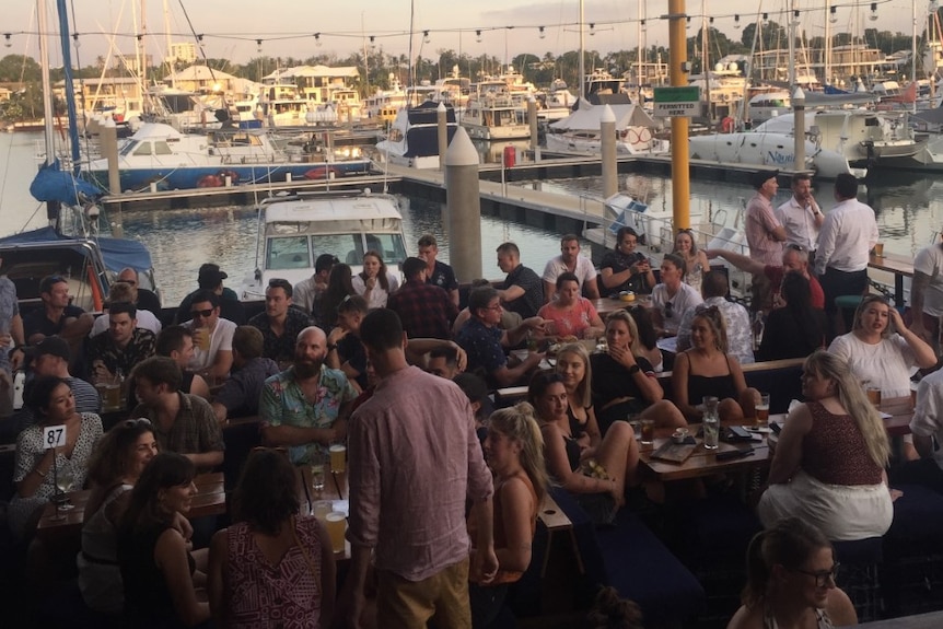 Groups of people sit at an outdoor waterfront restaurant in Darwin.