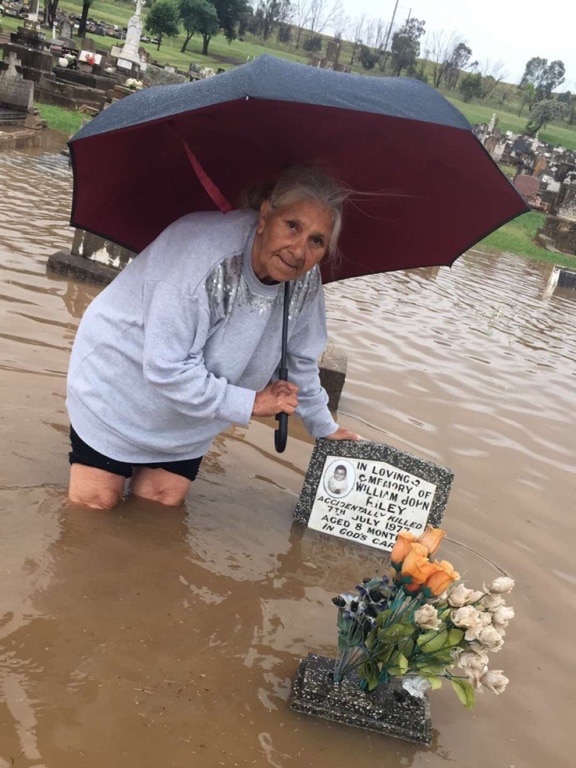 A woman stands in knee deep water, touching a grave marker stone