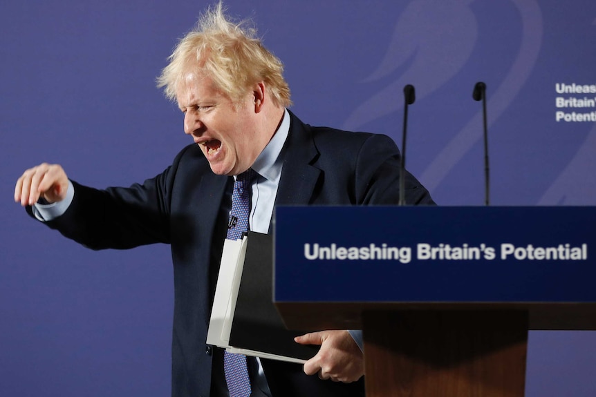 Boris Johnson gestures with his eyes closed in front of a lectern with words 'unleashing Britain's potential'.