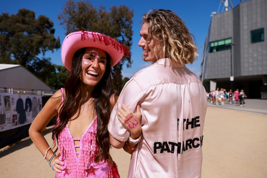 A young woman in a pink outfit smiles as her partner shows the back of his pink shirt.