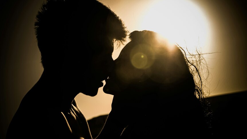 A photo of a couple kissing each other in silhouette against a bright light