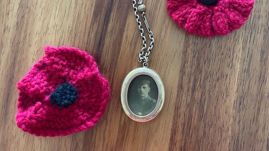 two crocheted red poppies sit beside a heavy locket with a photo inside. 