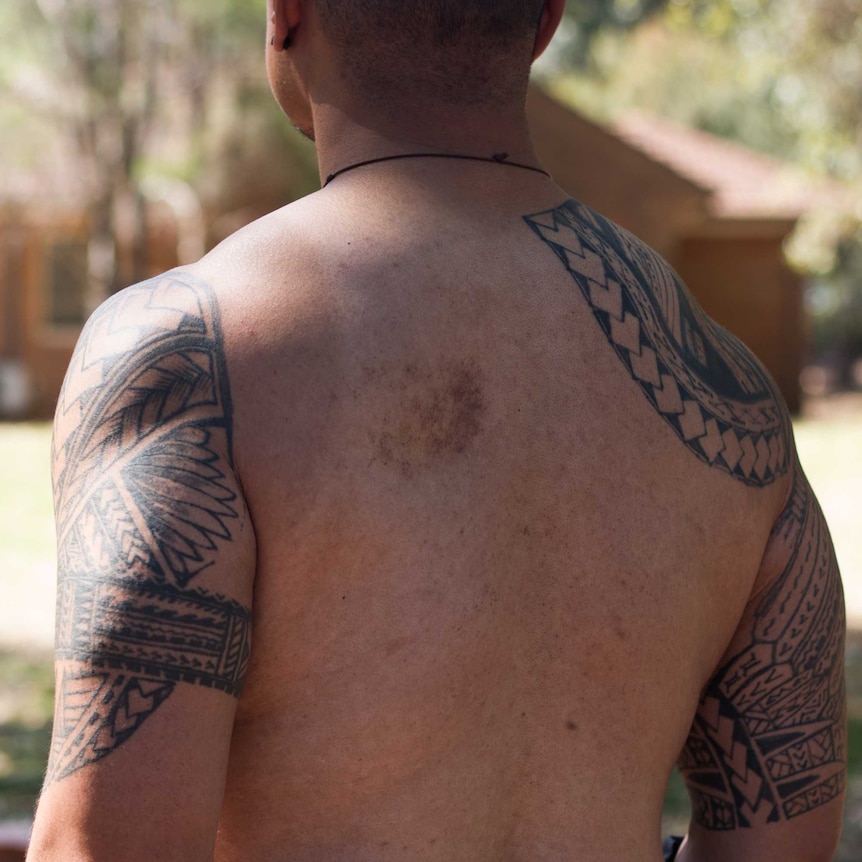 Shirtless back of Uniting Church Reverend Fie Marino. Tattoos on arms.