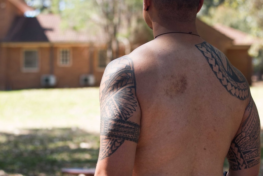 Shirtless back of Uniting Church Reverend Fie Marino. Tattoos on arms.
