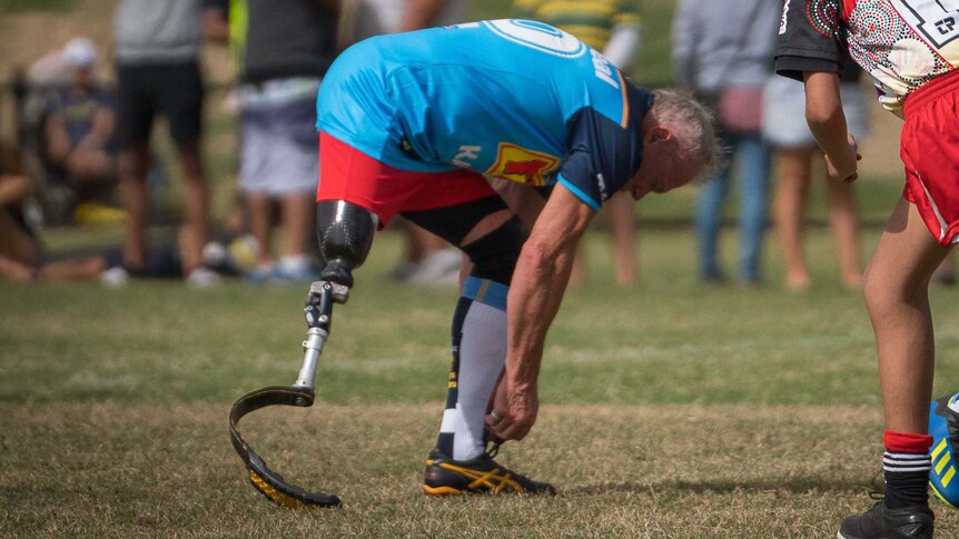 PDRL team player Todd Philpott bends down to tie his shoelace on the footy field. He wears a running prosthetic on one leg