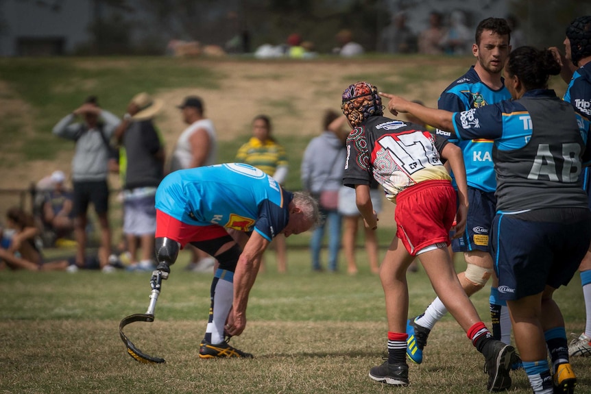 PDRL team player Todd Philpott bends down to tie his shoelace on the footy field. He wears a running prosthetic on one leg