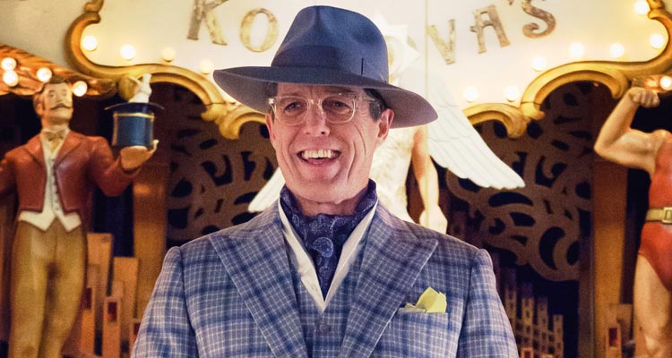 Hugh Grant in purple suit and hat laughing. 