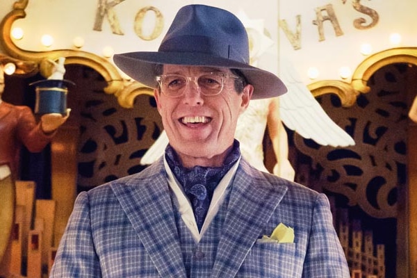 Hugh Grant in purple suit and hat laughing. 