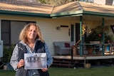 Bronte Harris standing in her yard holding a photo of her house during a flood in 2010.