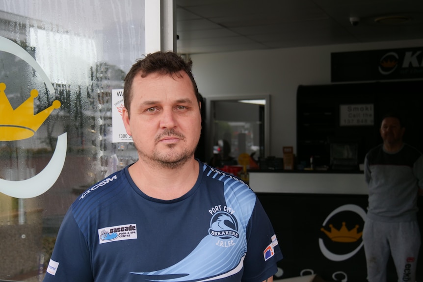 A man in a rugby league jersey standing outside his business looking sad