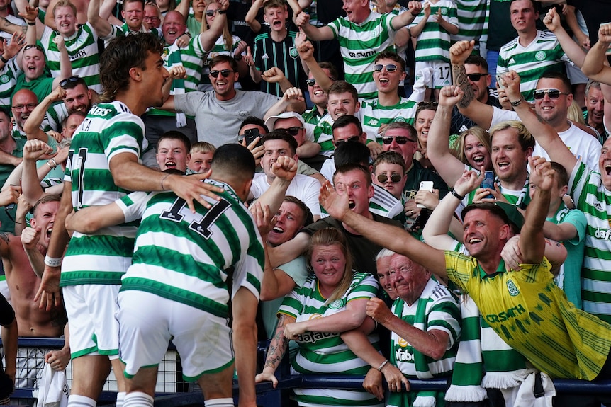 People in green and white striped shirts cheer together, holding their arms up in celebration.