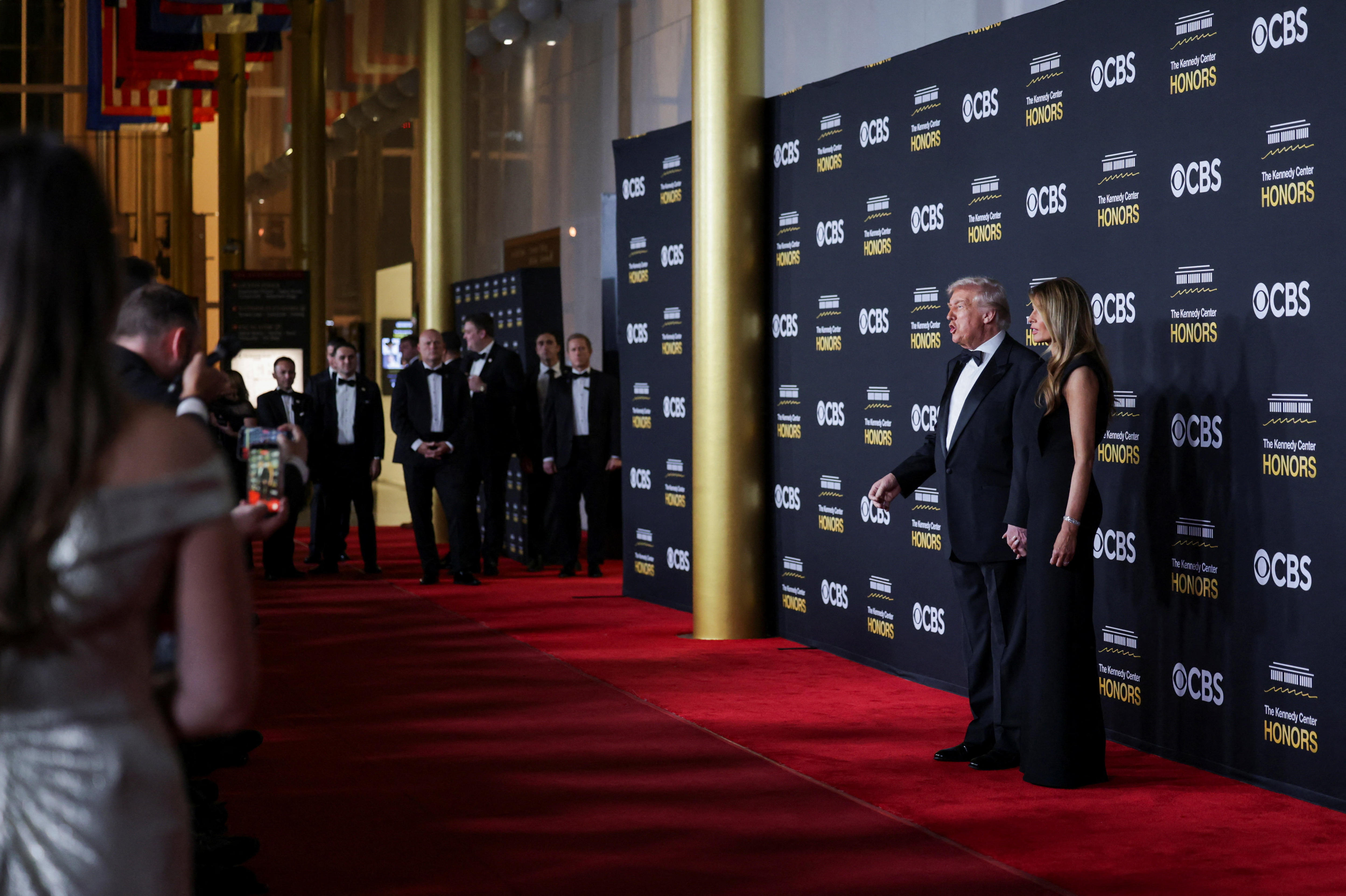 Donald y Melania Trump posan vestidos formalmente en una alfombra roja frente a los fotógrafos que les toman fotos.