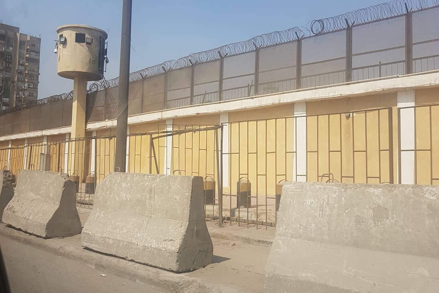 The view of Tora prison from the street outside. There are concrete barricades and barb wires on the walls.