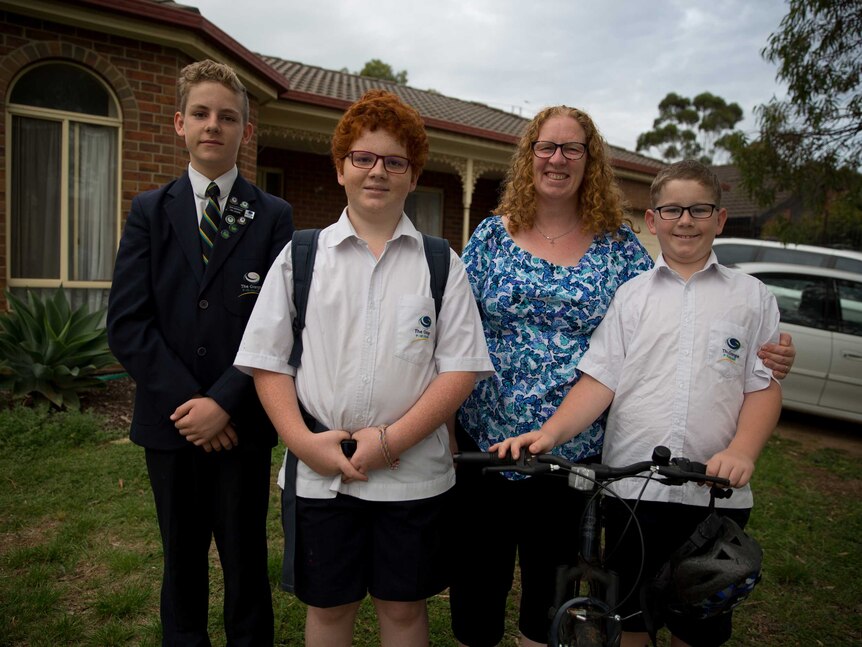 Mum Janet stands in front of her brick home with her arms around her boys