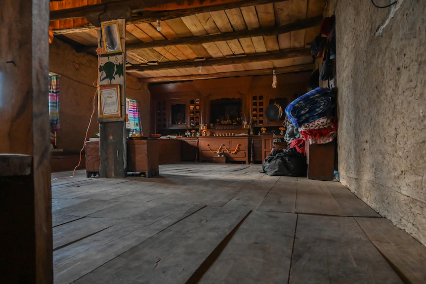 Inside a house with wooden floor and walls and household objects like blankets stacked against the wall