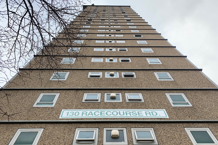 The exterior of a large public housing tower block with a sign saying '130 Racecourse Rd'.