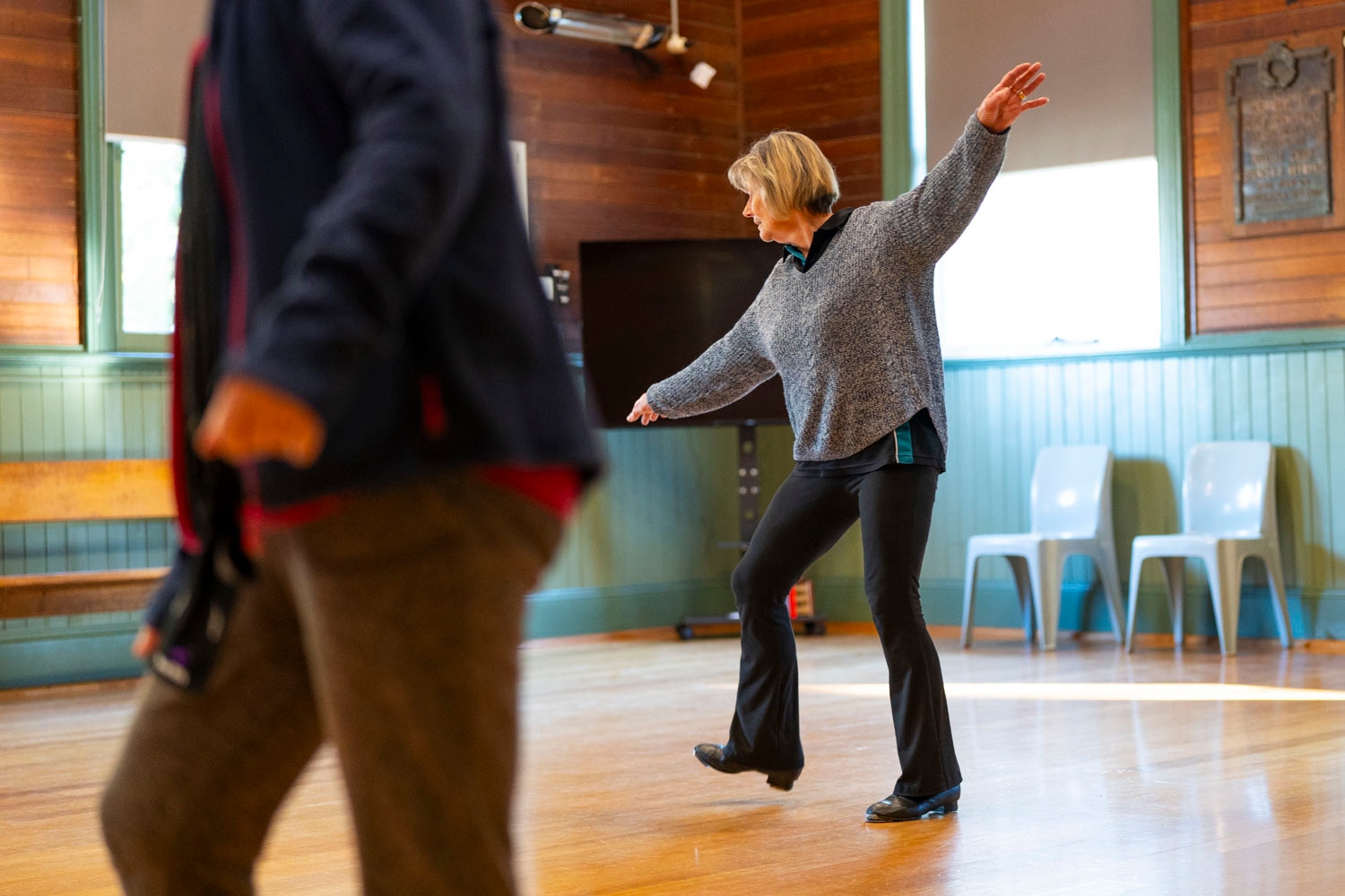 women dance in tap shoes in black and teal shirts in a wooden town hall