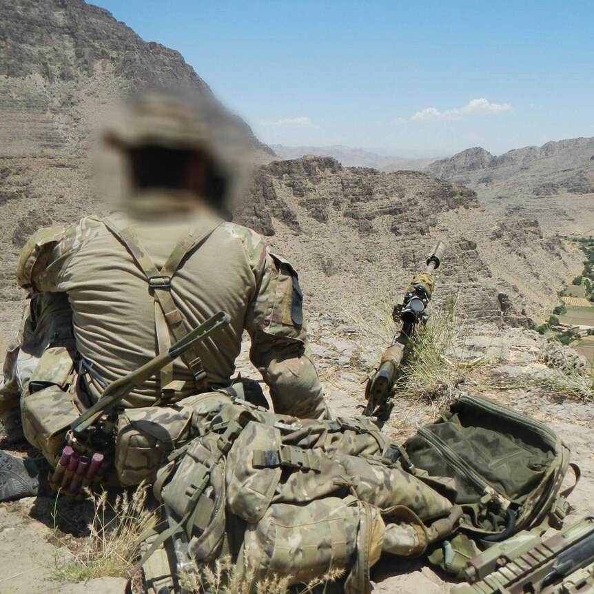 A soldier sits facing a valley in Afghanistan.